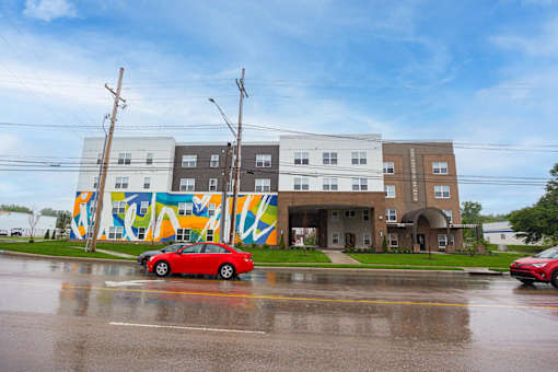 A red car is parked in front of a building with a colorful mural on the side.