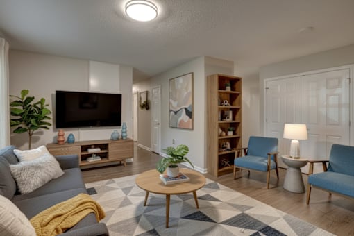 A living room with a grey couch, a wooden coffee table, a blue armchair, a bookshelf, and a television.