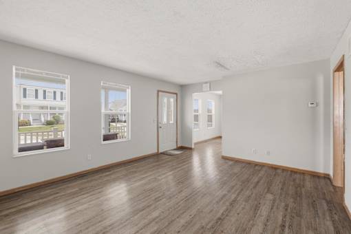 A spacious room with wooden floors and white walls, featuring two windows with pictures on them.