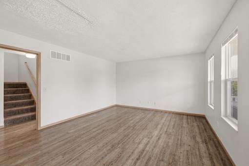 A room with wooden flooring and a staircase leading to another room.