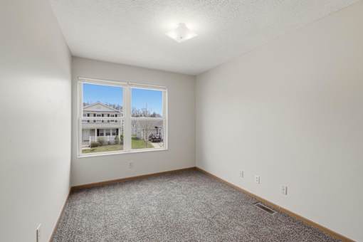 A room with a carpeted floor and a window showing a house across the street.