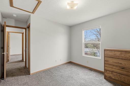 A room with a window, a picture on the wall, and a wooden dresser.