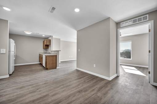 A spacious room with wooden flooring and a refrigerator in the corner.