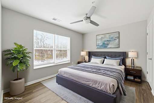 A bedroom with a large bed, a ceiling fan, and a potted plant.