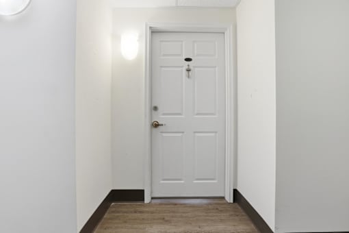 A white door with a keyhole and a doorknob is in a white room.