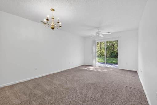A room with a carpeted floor, a chandelier, and a ceiling fan.