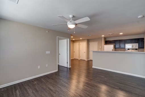 a living room with a ceiling fan and a kitchen in the background