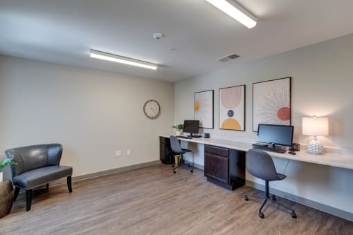 two computers on a long desk with a chair and a clock on the wall