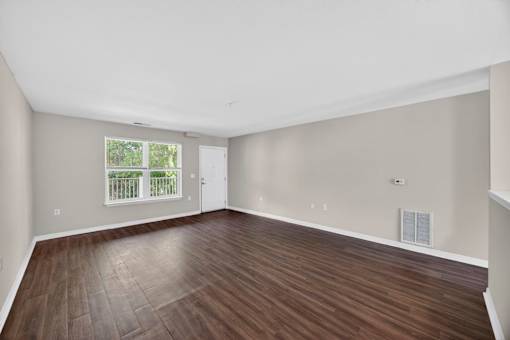 A room with wooden flooring and a window with a view of a fence.
