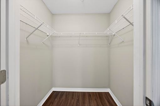 A walk-in closet with white shelving and a wooden floor.