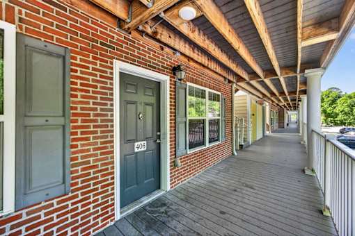 A long wooden porch with a brick wall and a door with the number 406 on it.