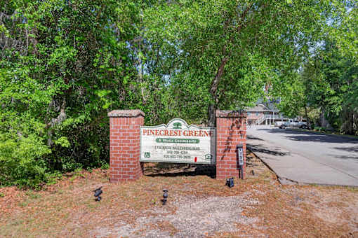 A sign for Pinecrest Green is surrounded by trees.
