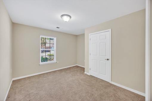 A room with a white door and a window with a view of a fence and trees.