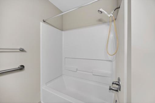 A white bathroom with a towel hanging on the shower rod.