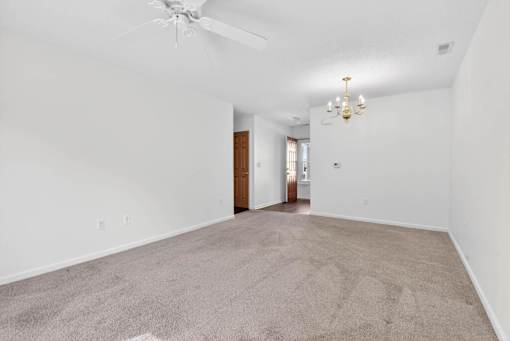 A spacious room with a carpeted floor and a chandelier hanging from the ceiling.