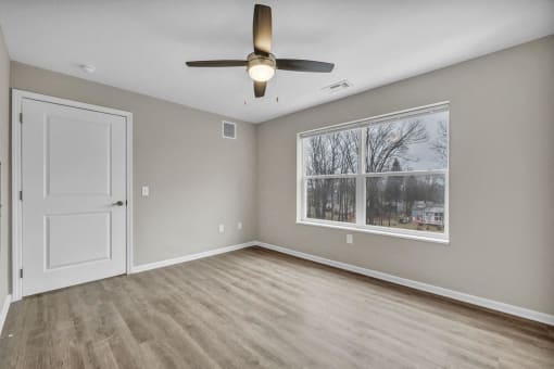 an empty living room with a large window and a ceiling fan