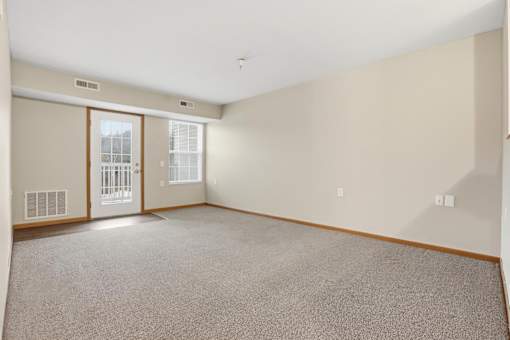 A large empty room with a carpeted floor and a door leading to a balcony.