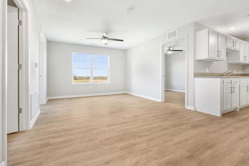 an empty living room with a kitchen and a ceiling fan