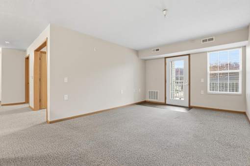 A large, empty room with a carpeted floor and a window with blinds.
