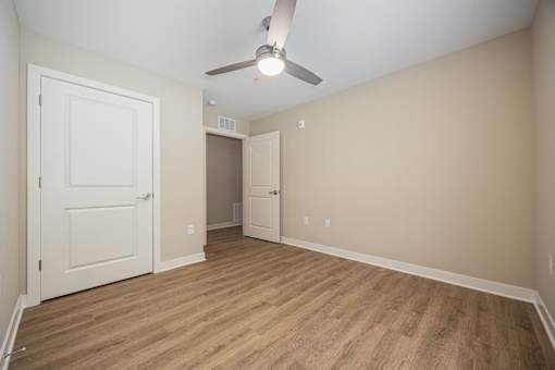 A room with a ceiling fan and light fixture, two doors, and a wooden floor.