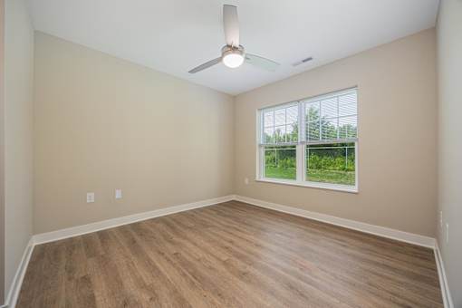 A room with a ceiling fan and a window overlooking a green area.