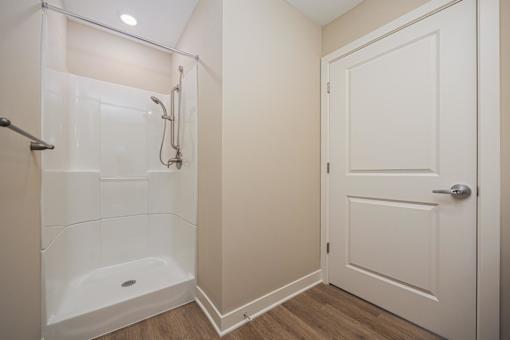 A white door is on the right of a bathroom with a walk in shower.