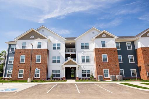 A large, modern apartment complex with a parking lot in front.