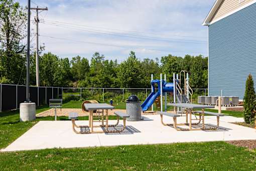 A playground with a slide, picnic table, and trash can.