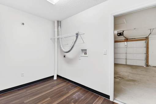 A room with a wooden floor and a white wall with a pipe running along it.
