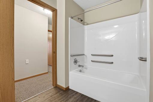 A white bathtub with a shower head and grab bars is in a bathroom.