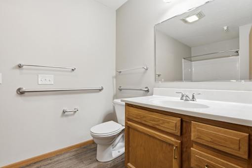 A white toilet sits in a bathroom with a white sink and wooden cabinets.