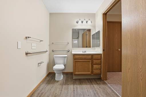 A white toilet sits in a bathroom with a wooden vanity and medicine cabinet.
