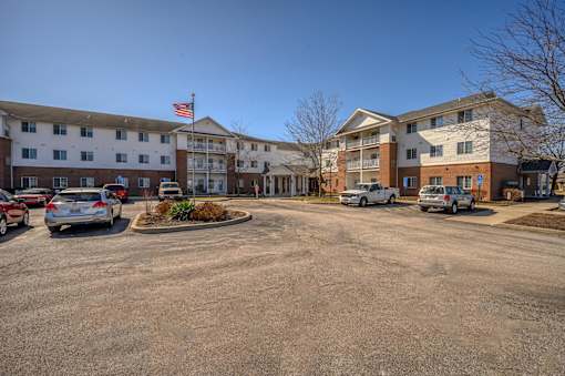 A parking lot in front of a multi-story apartment building with cars parked.