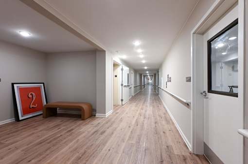 A long hallway with doors on both sides and a bench with a picture frame on the left.