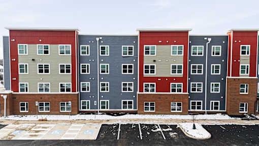 A row of apartment buildings with a parking lot in front.