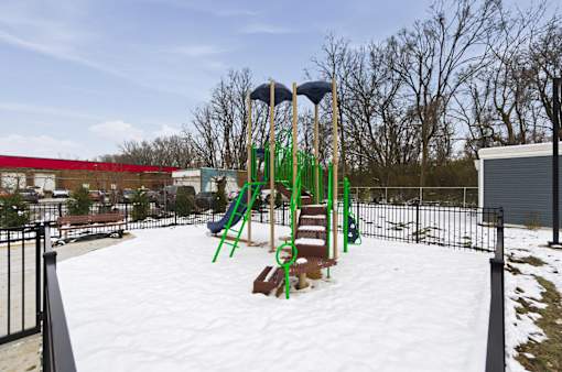 A playground with a green slide and a red building in the background.