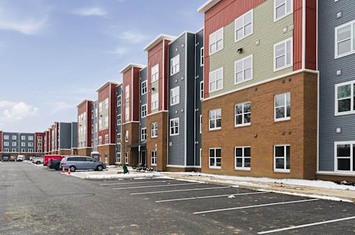 A row of multi-story apartment buildings with a parking lot in front.