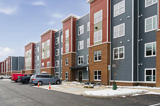A row of apartment buildings with cars parked in front.