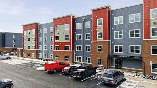 A parking lot with cars and a red truck in front of a row of apartment buildings.