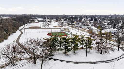 A snowy landscape with a winding road and a few trees.