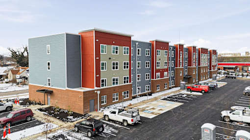 A row of multi-story buildings with cars parked in front.