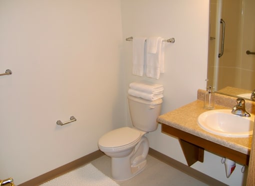 A white toilet is in a bathroom with a sink and towel rack.