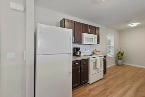 A white refrigerator stands in a kitchen with wooden cabinets and a white stove.