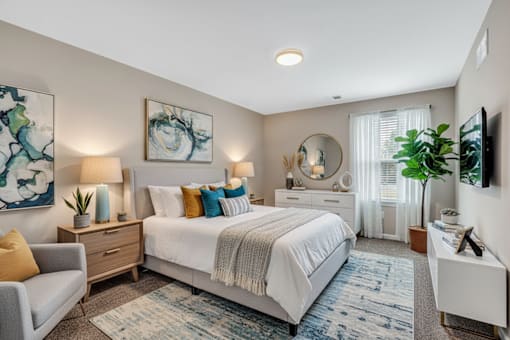 A bedroom with a large bed, a grey couch, and a painting on the wall.