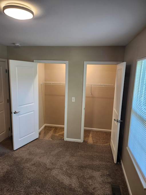 A room with two open closets and a carpeted floor.
