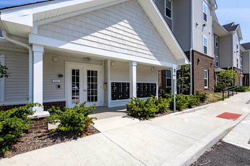 A white house with a porch and a red stop sign on the sidewalk.