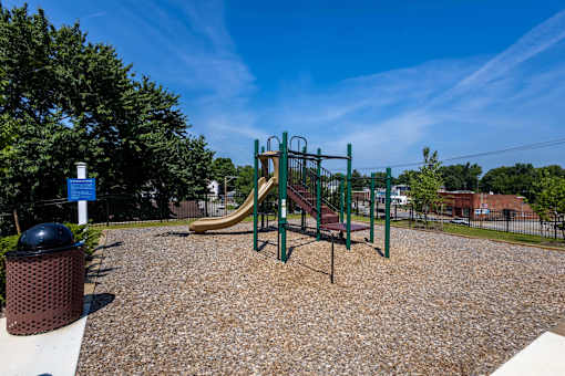 A playground with a slide, swings, and a trash can.
