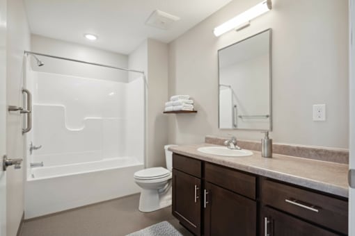 A white toilet sits in a bathroom next to a sink and a bathtub.