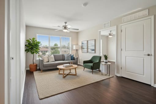 A living room with a grey couch, a green armchair, a wooden coffee table, and a ceiling fan.