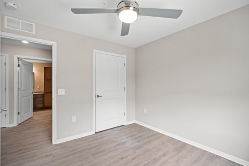 an empty living room with a ceiling fan and a door to a bedroom
